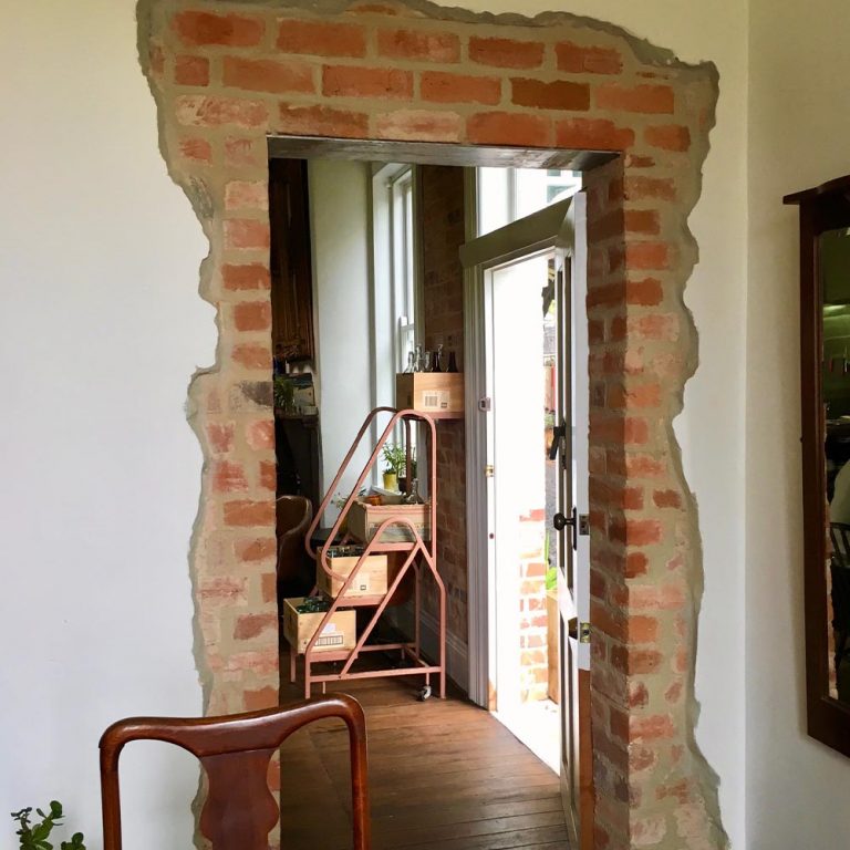 A rustic exposed brick doorway surrounded by clean white plaster walls